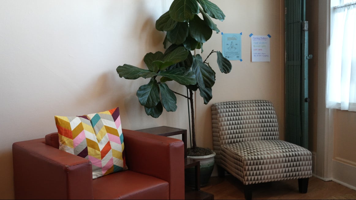 The lounge nook at Our Space Berkeley — red leather chair with colorful pillow, fiddle-leaf fig, patterned armchair