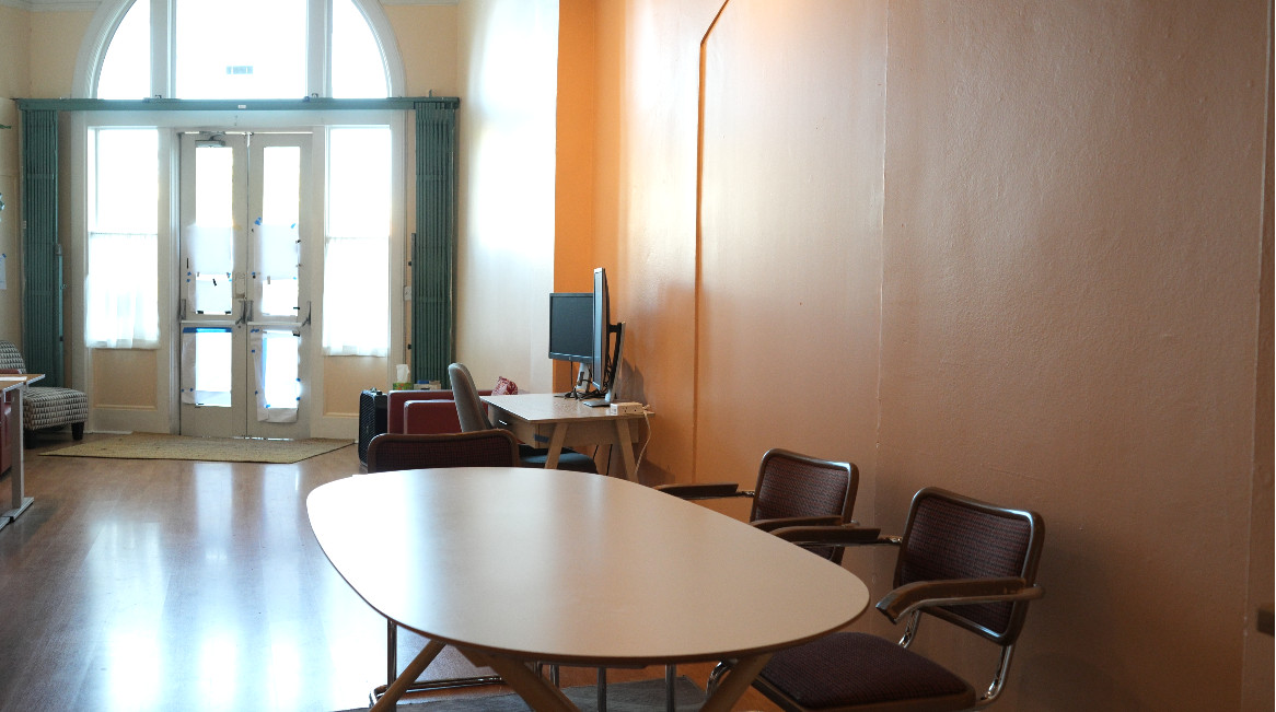 The main coworking room at Our Space Berkeley — round meeting table with Cesca chairs, arched front windows, hot desk with monitor