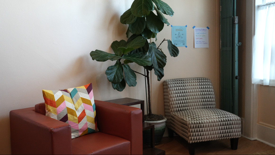 The lounge nook at Our Space Berkeley — red leather chair with colorful pillow, fiddle-leaf fig, patterned armchair